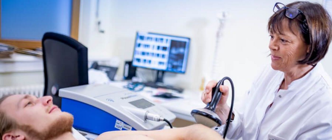 Ärztin behandelt Arm eines Patienten mit Stoßwellentherapie