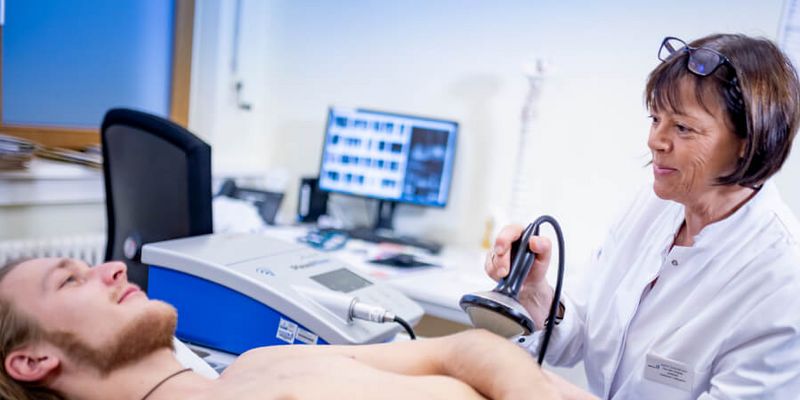 Ärztin behandelt Arm eines Patienten mit Stoßwellentherapie